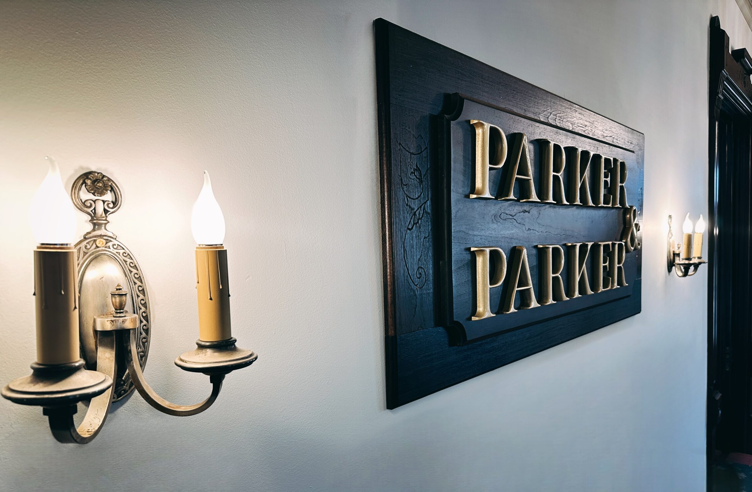 Hand-carved wooden Parker and Parker wall plaque with gold lettering flanked by brass candelabra sconces